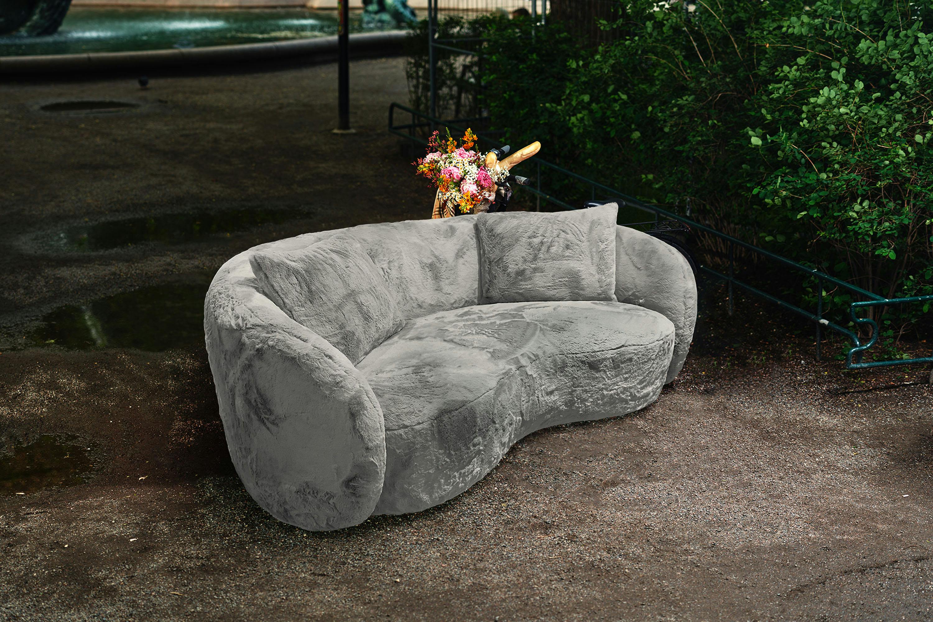 Grå loungesoffa i mjukt, fluffigt tyg. En nätt soffa med svängd, rundad form. Perfekt för salong eller lobby.