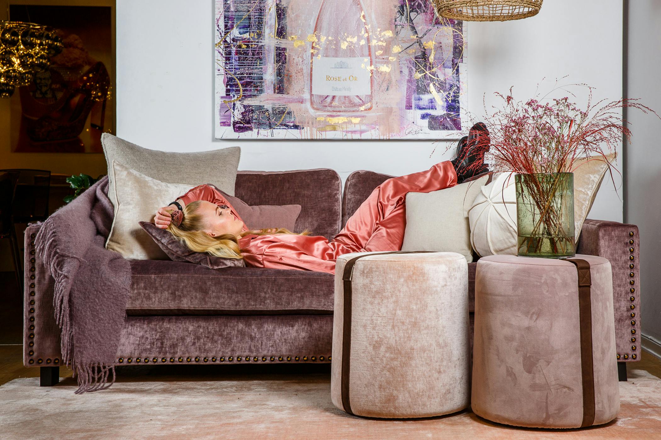 Djup 3-sits soffa med lyxig bomullssammet i lila kulör och med svartguldiga nitar längs stommen. 40x50cm stor, rund fotpall i bomullssammet och polyestersammet med band i brun anilinskinn.